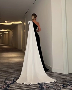 Detail van elegante zwarte een-schouder jurk met een lange witte vloeiende cape