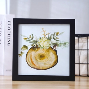 Close-up of a minimalist black square frame with botanical tree ring art on a wooden table