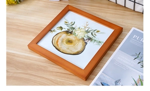 Detail view of a square light brown solid wood photo frame with botanical art on a wooden table