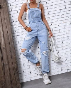 Detail of light blue distressed denim overalls with ripped knees and adjustable straps