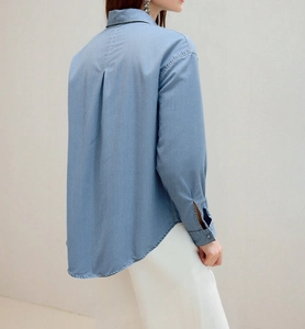 Detailed back view of a light blue denim shirt showing back pleats and curved hemline