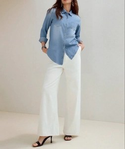 Detail view of light blue denim shirt with double chest pockets and high-waist white pants