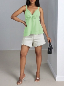 Détail d'un caraco vert clair à volants et d'un short en jean blanc à franges