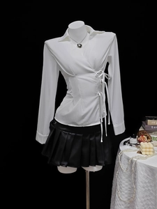 Detail of white wrap shirt with side tie bow and black pleated PU leather mini skirt