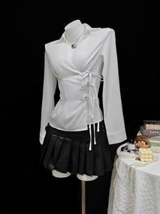 Detail of white wrap shirt with side waist bow ties and black pleated leather skirt