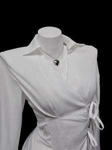 Close-up of a silver heart pendant necklace on a model wearing a white wrap shirt
