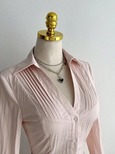 Detail of pink long-sleeve pleated shirt with V-neck and delicate button closure