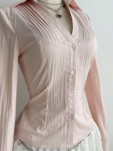 Detail of light pink long sleeve blouse with pleated V-neckline and textured fabric