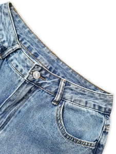 Dettaglio jeans blu chiaro con bottone metallico, passanti per cintura e tasche curve