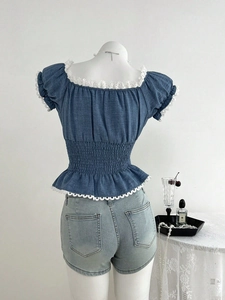 Top blu con maniche a sbuffo, bordo in pizzo e vita a punto smock su un manichino