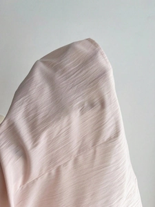 Close-up of light pink textured fabric showing detailed stitching and fine material grain