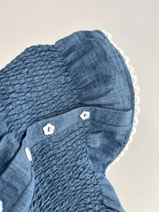 Dettaglio di tessuto plissettato blu con bordo in pizzo bianco e bottone a fiore
