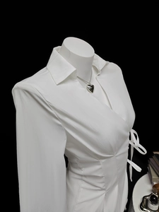 Detail of white satin wrap shirt showing elegant side-tie knot and waist ruching texture