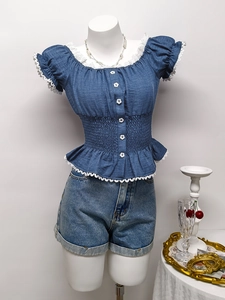 Dettaglio della camicetta in denim blu con pizzo bianco, bottoni a fiore e vita elastica