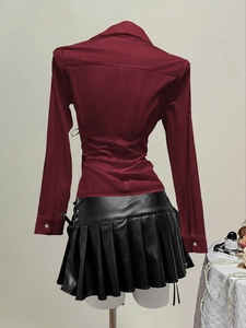 Rear view of a red long-sleeve shirt and black leather pleated skirt on a mannequin