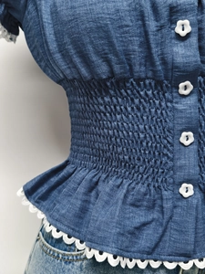 Dettaglio della vita a punto smock e bottoni floreali sul top blu a maniche corte