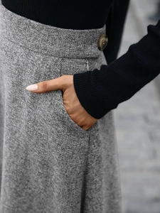 Detail of grey wool blend skirt showing textured fabric, amber button, and side pocket