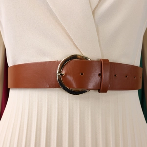 Detail eines eleganten braunen Ledergürtels mit großer goldener Schnalle am Kleid
