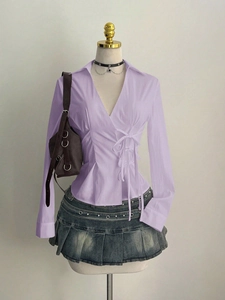 Detail of waist-tie design on light purple blouse and pleated denim skirt with belt