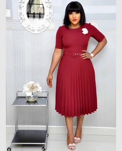 Detailed view of wine red pleated dress featuring a white floral brooch and waist belt