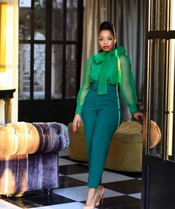 Women's chic green sheer bow blouse and high-waisted trousers set in elegant interior