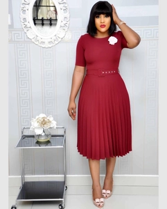 Detail of burgundy pleated dress featuring a round neck, waist belt, and white floral brooch