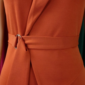 Detail of burnt orange jumpsuit waist with adjustable silver D-ring belt and twill fabric