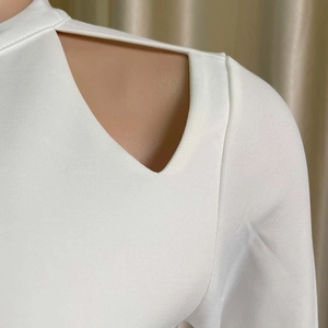 Dettaglio del top bianco a collo alto con ritagli geometrici sulle spalle