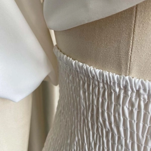 Detail of white smocked fabric and elastic pleated texture on the waist of a garment