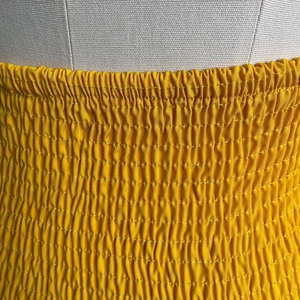 Detailed close-up of smocked elastic waist craftsmanship on ginger yellow garment