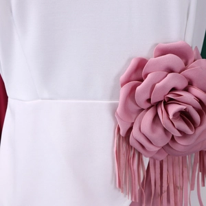Close-up of pink fabric rose and long tassel detail on white pleated dress waistline
