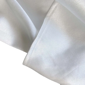 Détail du tissu en satin blanc montrant les coutures de l'ourlet et la texture soyeuse