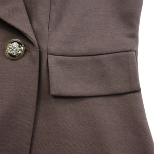 Détail du tissu marron de la robe avec poche à rabat et bouton doré à armoiries