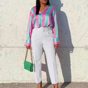 Detail of high-waisted white dress trousers paired with a green striped satin shirt and belt