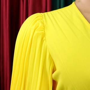 Détail d'une robe jaune élégante avec col en V, manches bouffantes plissées et tissu brillant