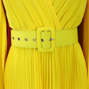 Détail d'une robe longue plissée jaune vif avec une large ceinture à œillets métalliques