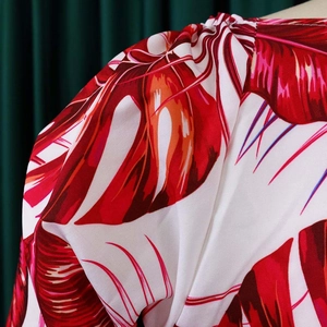 Détail de l'imprimé feuille tropicale rouge sur tissu tissé avec plis à l'épaule