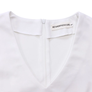 Detailed view of deep V-neckline with invisible zipper on textured white dress fabric