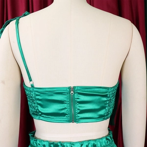 Close-up of emerald green satin top featuring rear metal zipper and side elastic pleats