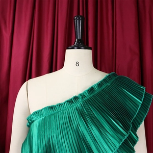 Detailed macro view of emerald green pleated one-shoulder top with ruffled texture