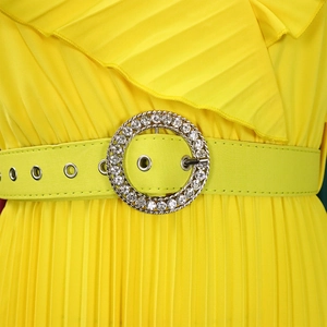 Détail d'une robe plissée jaune avec une ceinture verte et une boucle en strass