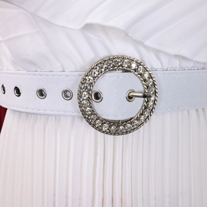 Gros plan détaillé de la ceinture blanche avec boucle strass sur une robe plissée