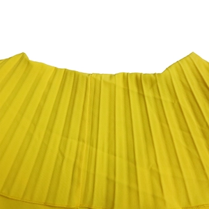 Détail de la jupe plissée jaune vif montrant la texture fine des plis accordéon