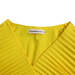Détail de la robe jaune à col en V avec texture plissée fine et étiquette de taille