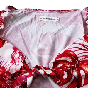 Détail du haut à imprimé tropical rouge et blanc avec volants et nœud au décolleté