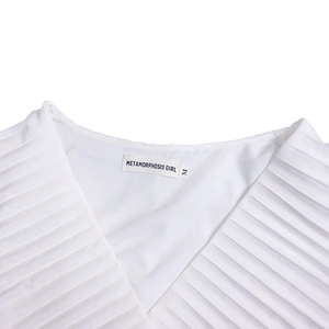 Détail du haut blanc à col en V montrant le plissé et l'étiquette METAMORPHOSIS GIRL