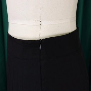 Detail of high waisted pleated trousers featuring a concealed back zipper on a mannequin