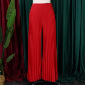 Detail of red high-waisted pleated wide-leg pants showing premium texture and drape