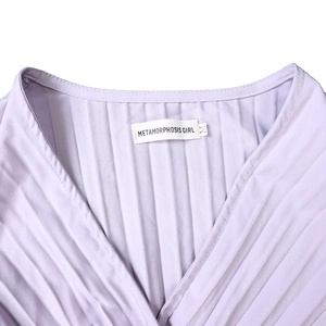 Détail d'une robe plissée lilas avec col en V, étiquette et texture de tissu fine