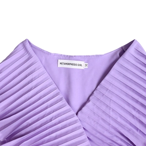 Détail du tissu plissé violet avec col en V et étiquette de marque blanche sur la robe